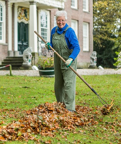 Vrouw harkt bladeren bij elkaar met hark op grasveld op Landgoed Huys Ten Donck
