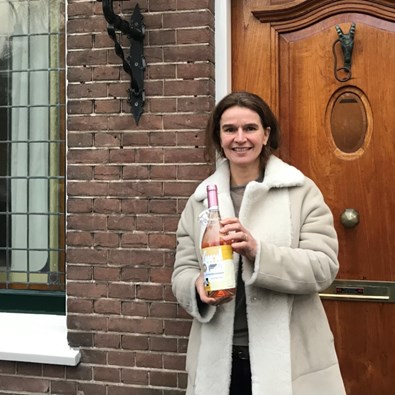 Vrouw met fles champagne in hand voor bakstenen huis met houten voordeur