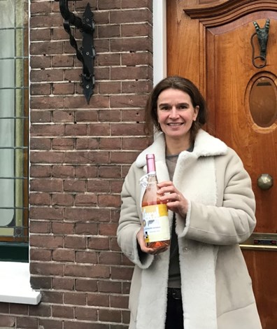 Vrouw met fles champagne in hand voor bakstenen huis met houten voordeur