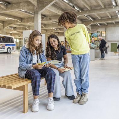 Drie kinderen in het FENIX museum, kijkend naar een schoolplaat/flyer