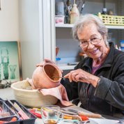 Vrouw zit aan tafel met gereedschap en aardewerken kruik