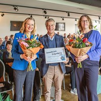 De uitreiking van Immaterieel Erfgoedprijs door voorzitter Erik Kopp (midden) aan Ellen Steendam (links) en Marloes Wellenberg (rechts) met een oorkonde en bloemen.
