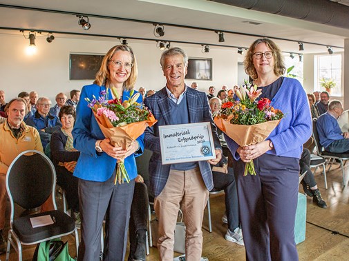 De uitreiking van Immaterieel Erfgoedprijs door voorzitter Erik Kopp (midden) aan Ellen Steendam (links) en Marloes Wellenberg (rechts) met een oorkonde en bloemen.
