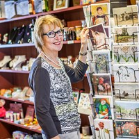 Vrouw met bril staat in winkel en pakt kaart uit kaartenrek