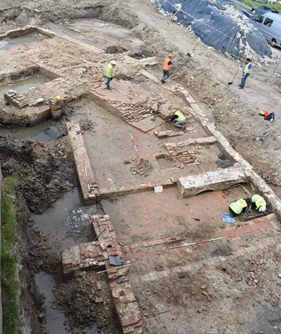 Archeologische put met restanten van muren van een kloostergebouw en archeologen aan het werk