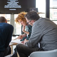 Foto vorige bijeenkomst: drie deelnemers kijken naar een oprdacht.
