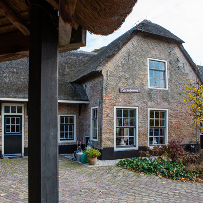 Foto van een historische boerderij met melkbussen naast de deur