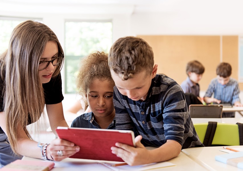Kinderen kijken met leraar in de klas op tablet