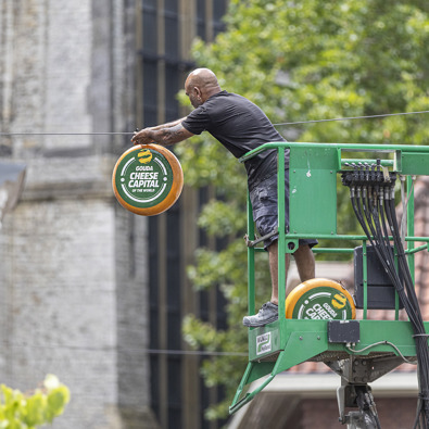 Man op hoogwerker hangt buiten een kaas op met de tekst: 