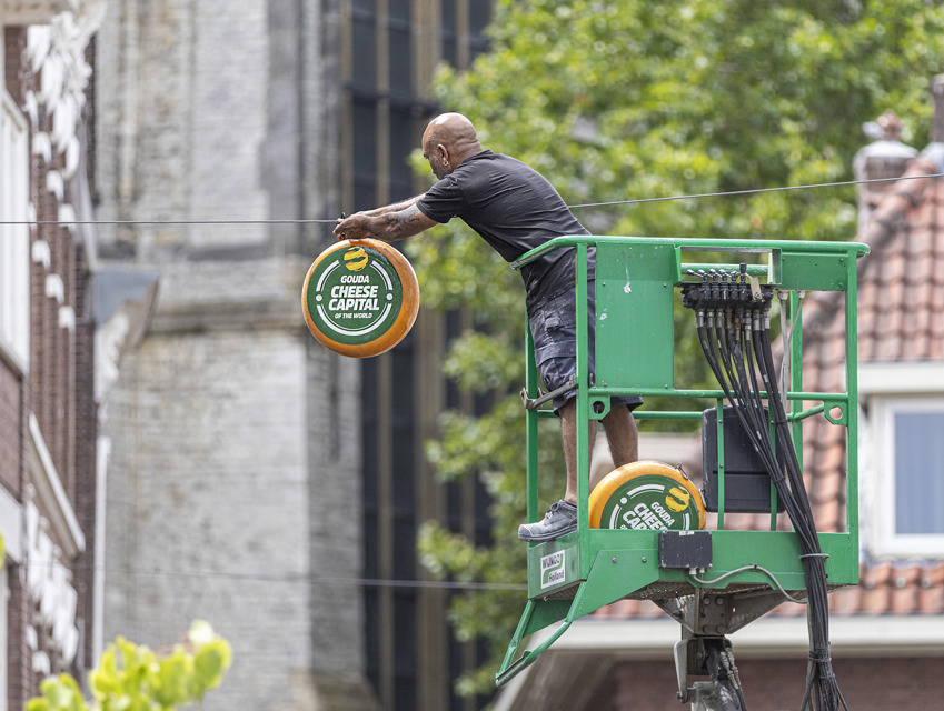 Man op hoogwerker hangt buiten een kaas op met de tekst: 