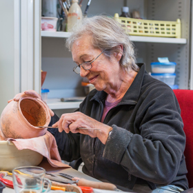 Vrouw zit aan tafel met gereedschap en aardewerken kruik