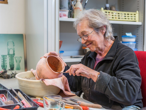 Vrouw zit aan tafel met gereedschap en aardewerken kruik