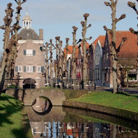 Gracht met gras en bomen en op achtergrond een monument