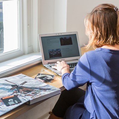 vrouw werkt op laptop achter bureau met boek en floppydisks naast zich