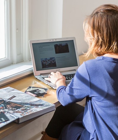 vrouw werkt op laptop achter bureau met boek en floppydisks naast zich