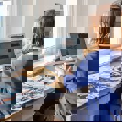 vrouw werkt op laptop achter bureau met boek en floppydisks naast zich
