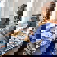 vrouw werkt op laptop achter bureau met boek en floppydisks naast zich