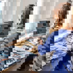 vrouw werkt op laptop achter bureau met boek en floppydisks naast zich