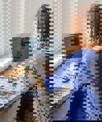 vrouw werkt op laptop achter bureau met boek en floppydisks naast zich