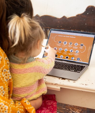 Foto van vrouw met kind en laptop. Op het beeldscherm is de Canon van Zuid-Holland te zien.