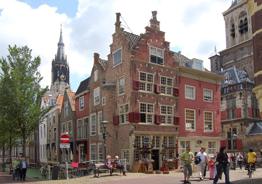 Mensen lopen op Oude Delft in Delft met op de achtergrond de Nieuwe Kerk