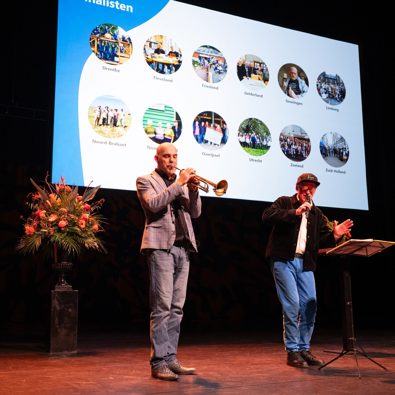 Op het podium twee muzikanten met op de achtergrond een scherm met de finalisten