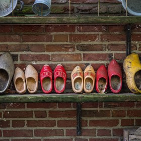 Houten klompen op een rij op een plank tegen bakstenen muur