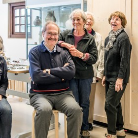 Twee mensen zitten op krukken en drie mensen staan in ruimte