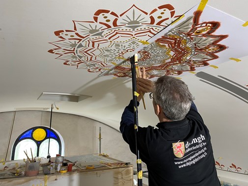 Man schildert met stencel een plafondschildering in een kerk